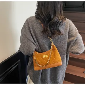 Detail of a brown suede hobo bag with quilted stitching and gold chain strap worn by a model