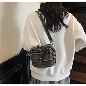 Detail of dark denim crossbody bag with multiple zippers and adjustable metal buckle strap