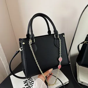 Sac à main chic noir motif litchi avec chaîne dorée et breloques fraises sur un livre