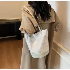 Dettaglio della borsa a secchiello crema con tracolle verde menta e motivi floreali