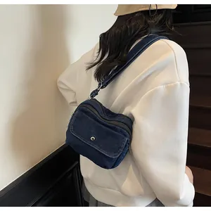 Detail of blue denim crossbody bag with silver buckle on white sweatshirt