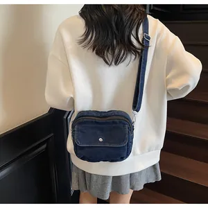 Detailed back view of a blue denim crossbody bag with adjustable wide strap on a model