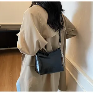 Detail of a black glossy leather shoulder bag with chain charm worn with a beige coat