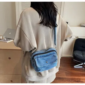 Blue denim crossbody bag featuring dual zipper compartments and front flap pocket detail