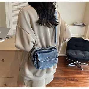Detail of blue denim crossbody bag featuring metal buckles and side zipper on a model