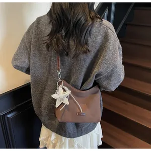 Brown frosted crescent shoulder bag with star charm detail shown on a wooden staircase