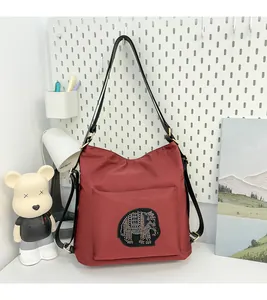 Detail of red-brown nylon tote bag featuring a sparkling elephant patch and gold hardware