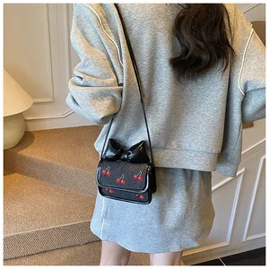 Close-up of black mini crossbody bag featuring cherry embroidery and leather bow detail