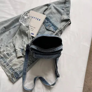Minimalist light blue denim crossbody bag with zipper closure shown on white fabric