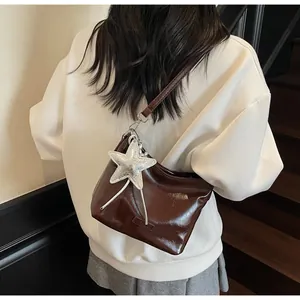 Detail view of glossy dark brown hobo bag featuring a metallic silver star pendant and ribbon