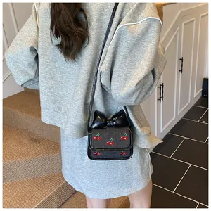 Detail of mini crossbody bag featuring a large black bow and red cherry embroidery