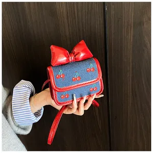 Close-up of mini blue denim bag with cherry embroidery and a large red bow detail