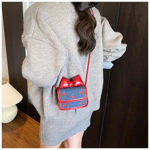 Close-up of mini blue denim crossbody bag featuring cherry embroidery and red bow detail