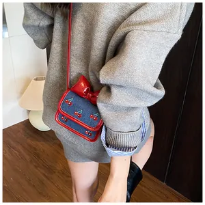 Mini denim crossbody bag with red bow and cherry embroidery shown on a young model