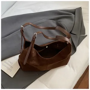 Brown matte suede hobo bag on grey blazer with adjustable shoulder strap and silver buckles
