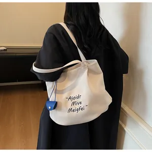 Detail of off-white canvas tote bag with blue charm and black artistic lettering