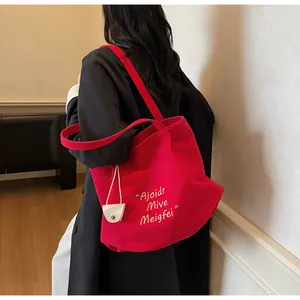 Detailed view of a red canvas tote bag with white lettering on a black coat outfit