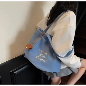 Blue canvas tote bag with white embroidery and side drawstring detail on person