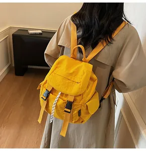 Detail of yellow canvas backpack with black buckle and drawstring on a beige trench coat