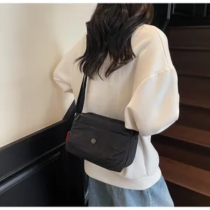 Close-up of minimalist black nylon crossbody bag with side red tag on a person