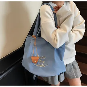Detail of blue canvas tote bag featuring beige embroidery and a brown leather charm