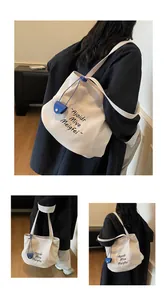 Detail view of cream canvas tote bag with contrast lettering and mini blue charm