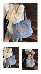 Detail of light blue canvas tote bag with yellow embroidery and small leather pouch