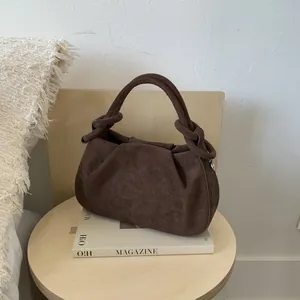 Dark brown pleated shoulder bag with unique knotted handle on a wooden stool setup