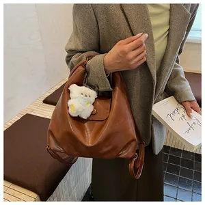 Sac à dos rétro en cuir marron foncé avec breloque ours, porté par un mannequin en intérieur