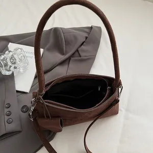 Minimalist dark brown suede underarm bag with cylindrical handle and sleek shoulder strap