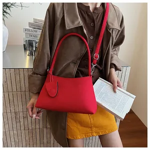 Detail of red faux suede shoulder bag with circular handle and thin strap on a model