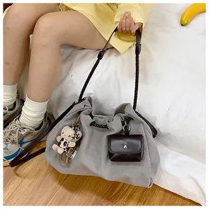 Detail of grey canvas hobo bag with woven strap, bear charm and mini leather pouch accessory