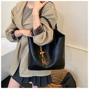 Detail of black faux leather tote bag with unique wood bead tassel and woven charm