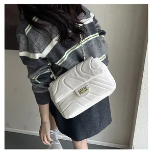 Gros plan d'un sac bandoulière blanc matelassé avec chaîne dorée porté par un mannequin