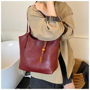 Detail of burgundy tote bag with pleated texture and beaded tassel charm on a model