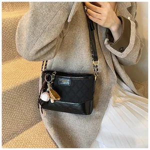 Detail of black quilted bucket bag with sporty baseball charms and chain strap