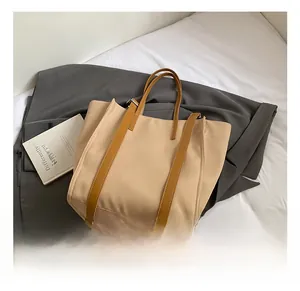 Detail view of large beige tote bag with brown leather straps on a minimalist background