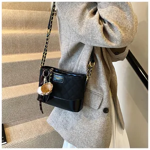 Detail of black quilted bucket bag featuring a gold chain and unique baseball charm
