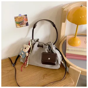 Macro detail of grey canvas bucket bag featuring woven handle and adorable bear pendant