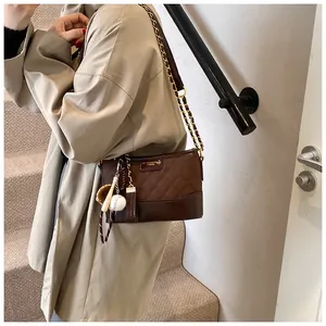 Detail of dark brown quilted bucket bag with vintage baseball themed charms and chain strap