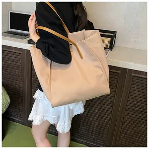 Close-up of a large beige tote bag with brown leather handles worn over the shoulder