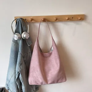 Close-up of pink frosted leather tote bag hanging on wooden hook with denim jacket