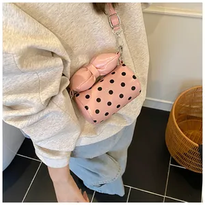 Detailed view of pink polka dot cylinder crossbody bag worn by a model in soft lighting
