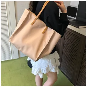 Spacious apricot nylon tote bag with brown handles being worn in a stylish indoor setting