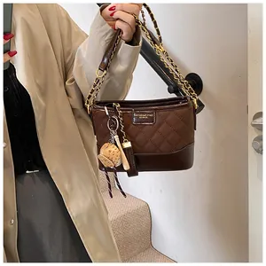 Detail of dark brown quilted bucket bag with gold chain strap and baseball charm