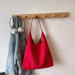 Detailed view of a red matte suede oversized hobo shoulder bag hanging on a wooden hook