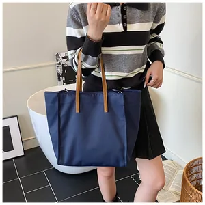 Navy blue nylon tote bag with brown leather handles shown in a lifestyle setting