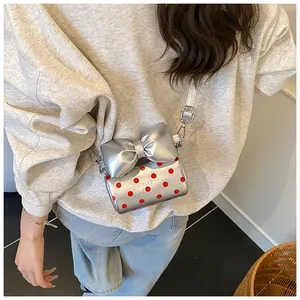 Close-up of a silver polka dot mini bag with a red bow on a female model with strap