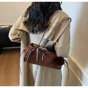 Braune Wildleder-Umhängetasche mit karierter Schleife und Plüschball-Anhänger am Model