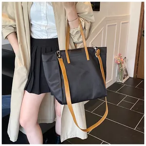 Detail of black tote bag with camel straps showing side pocket and adjustable crossbody strap